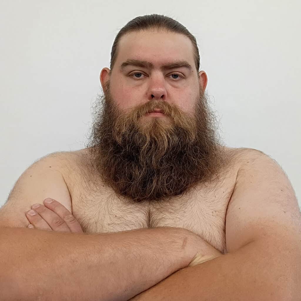 Sumo wrestler with long beard and crossed arms, shirtless, against a plain background.