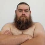 Sumo wrestler with long beard and crossed arms, shirtless, against a plain background.