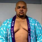 Sumo wrestler wearing a blue floral kimono with a purple sash.