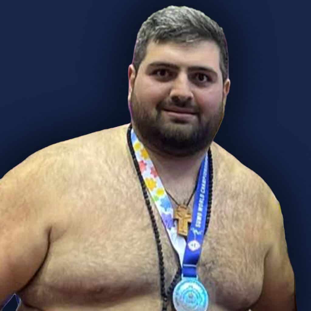 Sumo wrestler with medal and cross necklace on stage.