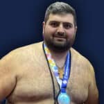 Sumo wrestler with medal and cross necklace on stage.