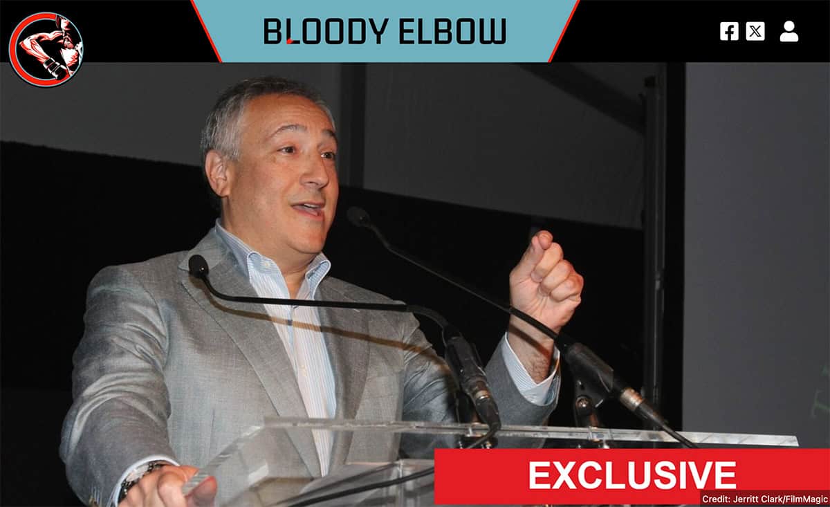 Ex-WWE president speaking at sumo league event with logo and social icons.