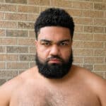 Close-up of Brandon Rudzinski with serious expression, bare shoulders, against brick wall.