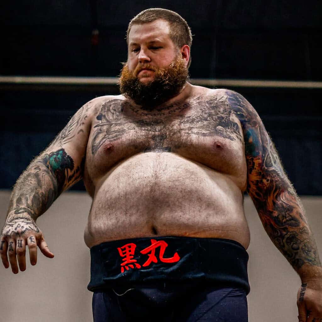 Sumo wrestler with tattoos and beard in training.