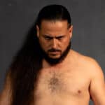 Sumo wrestler with long hair and beard looking serious.