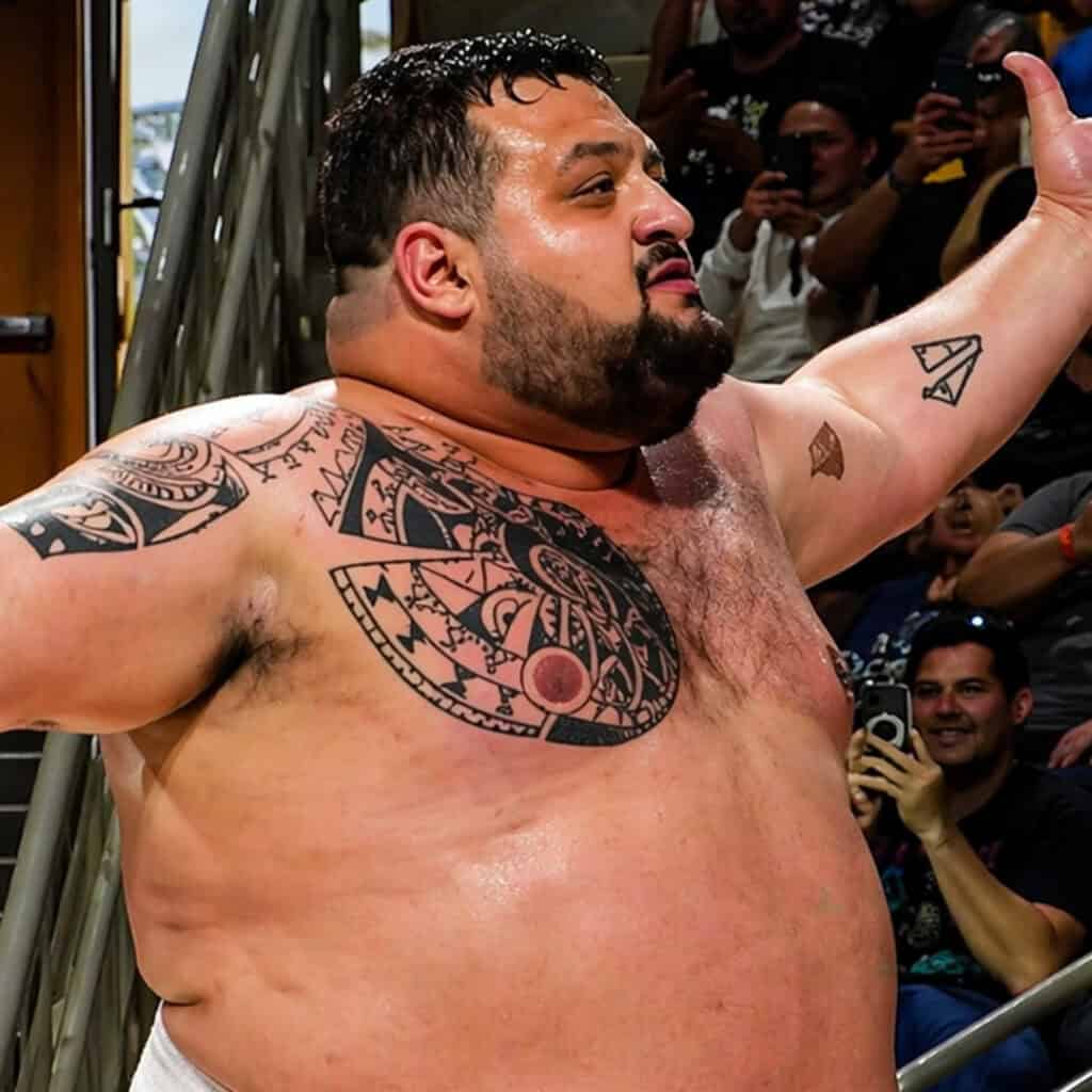 Sumo wrestler with tattoos raising his arm in victory.